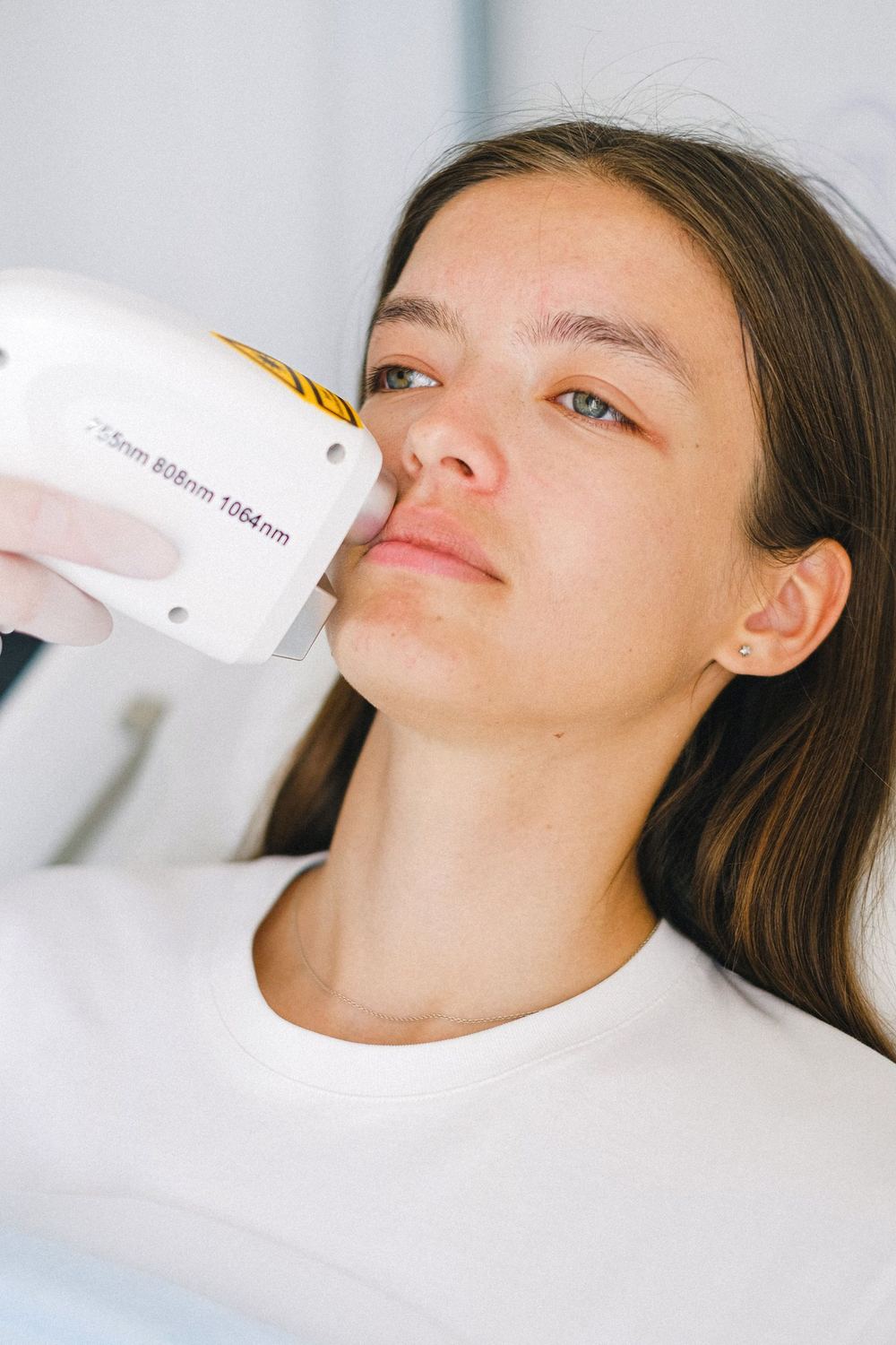 A light-based skin treatment handpiece being used on a client's face in a clinic.